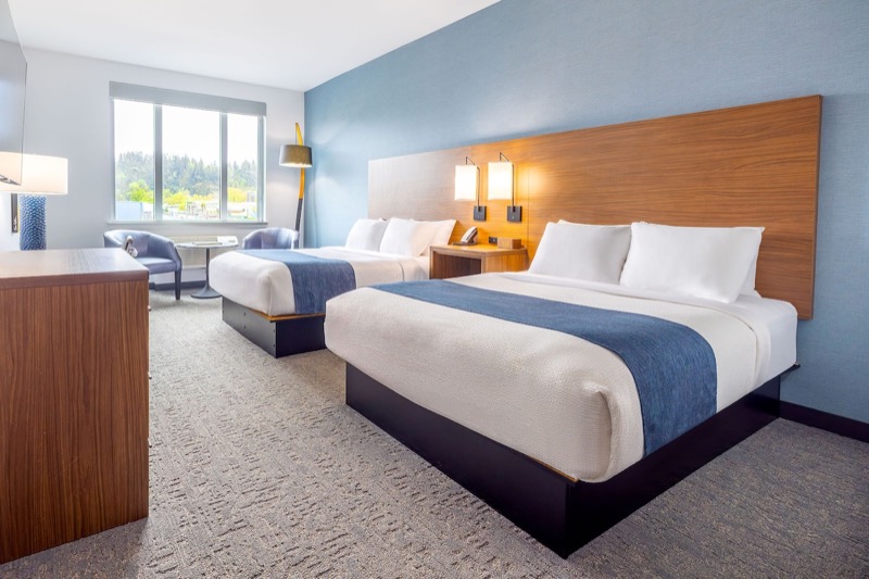 Deluxe Double Queen guest room with two queen beds, blue accent wall, wood headboard, and window seating
