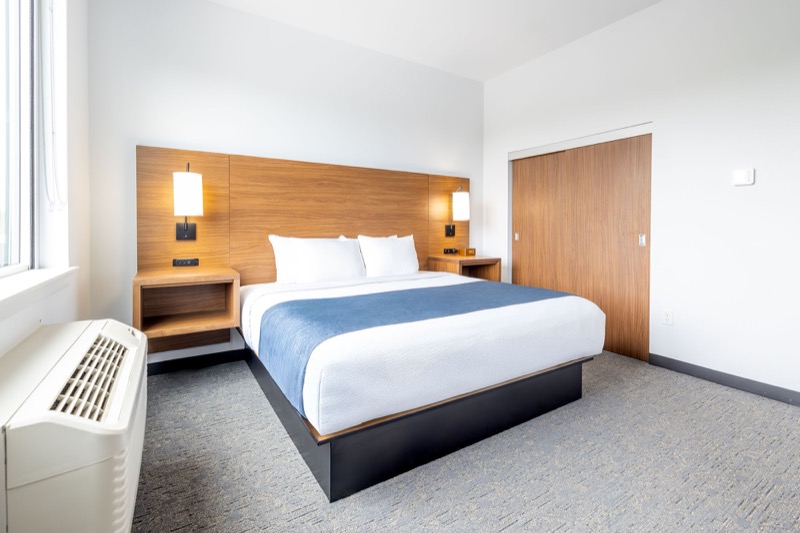 Deluxe Suite king bedroom with wood headboard, wall sconces, open nightstand shelves, window, and connecting suite door