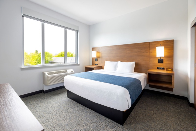 Deluxe Suite king bedroom with large window and treetop view, warm wood headboard with sconces, and floating nightstands