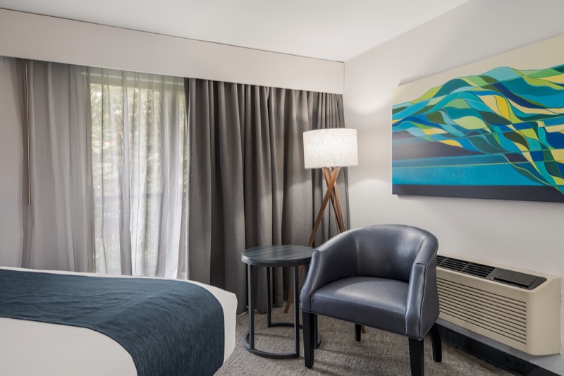 Double Queen room seating area with a blue leather armchair, round side table, tripod floor lamp, and abstract art above the AC unit