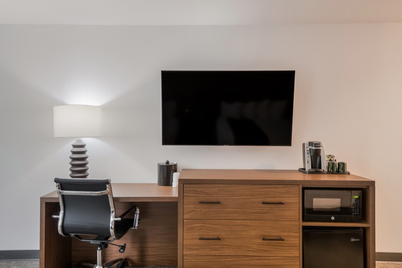 Double Queen room desk and dresser unit with wall-mounted TV, built-in microwave and mini-fridge, and coffee maker with green mugs