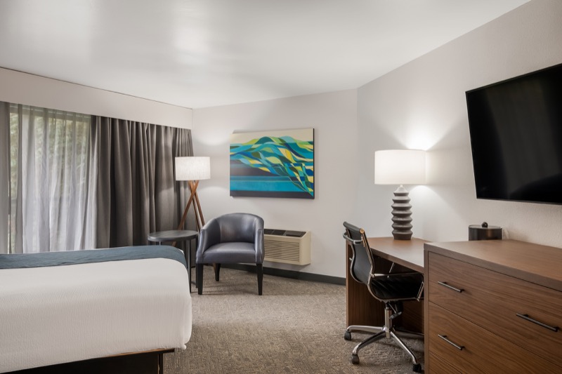 Double Queen room wide view showing window seating, abstract art, desk, dresser with TV, and corner of the beds