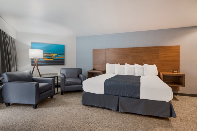 King Suite king bed with wood headboard, navy runner, two blue leather armchairs, tripod floor lamp, and abstract artwork