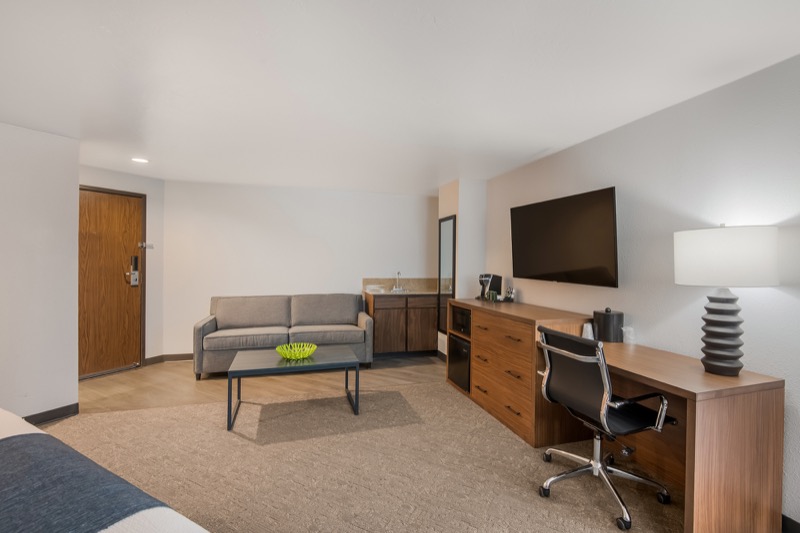 King Suite living area from the opposite angle, showing sofa, TV above dresser, office chair, desk lamp, and entrance door