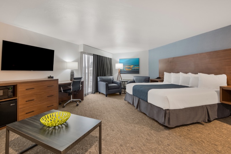 King Suite with king bed, two leather armchairs, wall-mounted TV, desk, window with curtains, and abstract landscape art