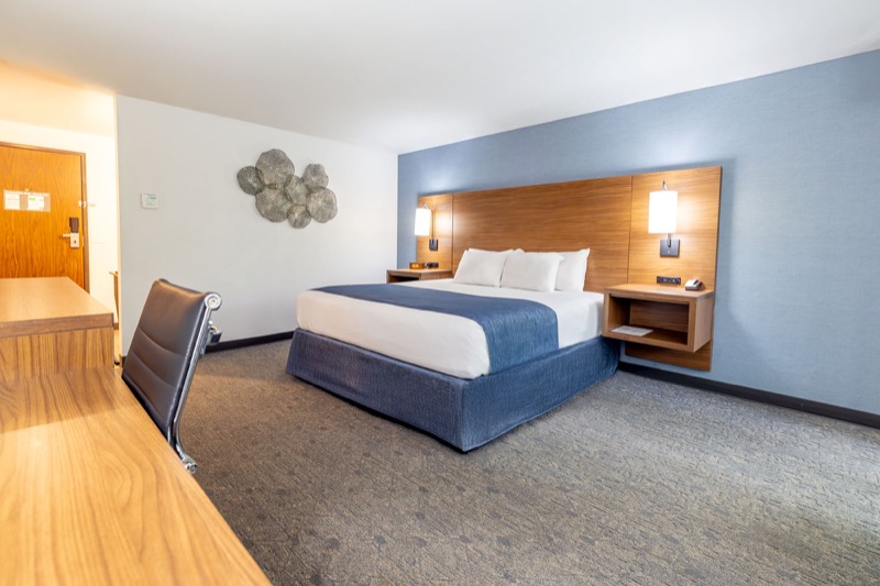 Waterview King guest room with king bed, blue textured accent wall, wood headboard with nightstands, desk, and black office chair