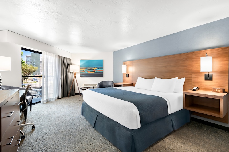 King guest room with king bed, light blue accent wall, wood headboard, balcony door, and seating area